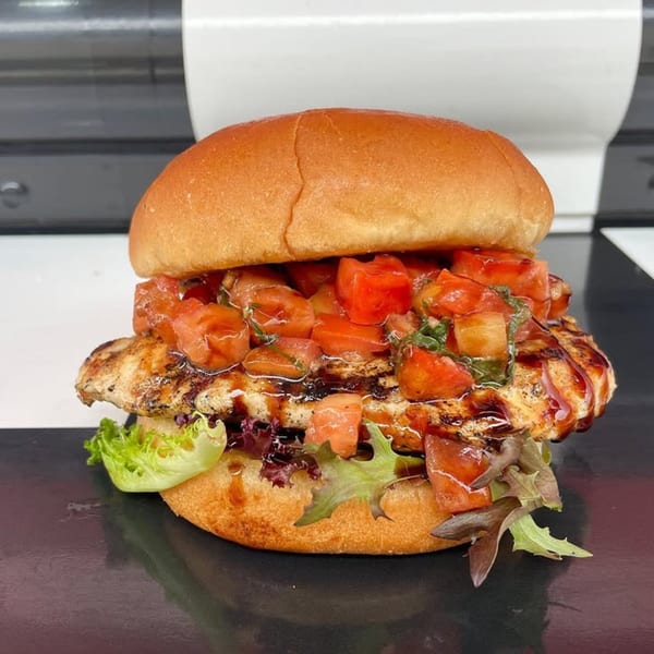 Rockin' Burgers' grilled chicken sandwich with diced tomatoes, basil, and balsamic glaze on a bun.
