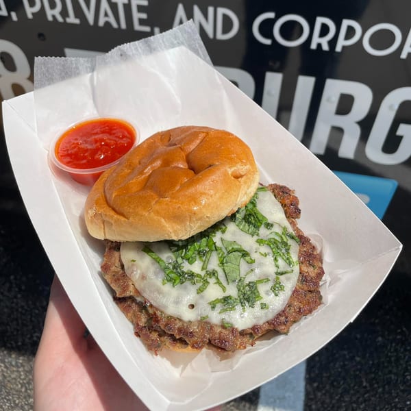 Rockin' Burgers' burger with melted cheese, basil, and a side of red sauce in a white tray.