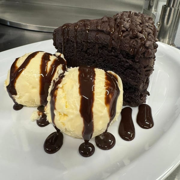 A slice of chocolate cake with chocolate chips and two scoops of vanilla ice cream with chocolate syrup.