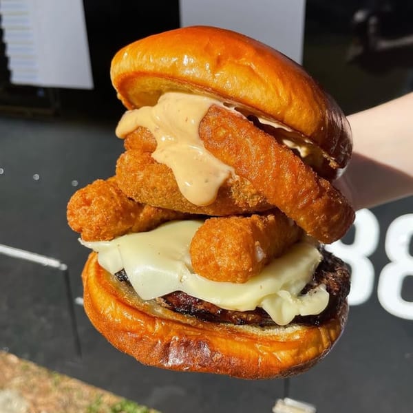 A Rockin' Burgers burger with a patty, melted cheese, and golden fried tater tots, drizzled with sauce.